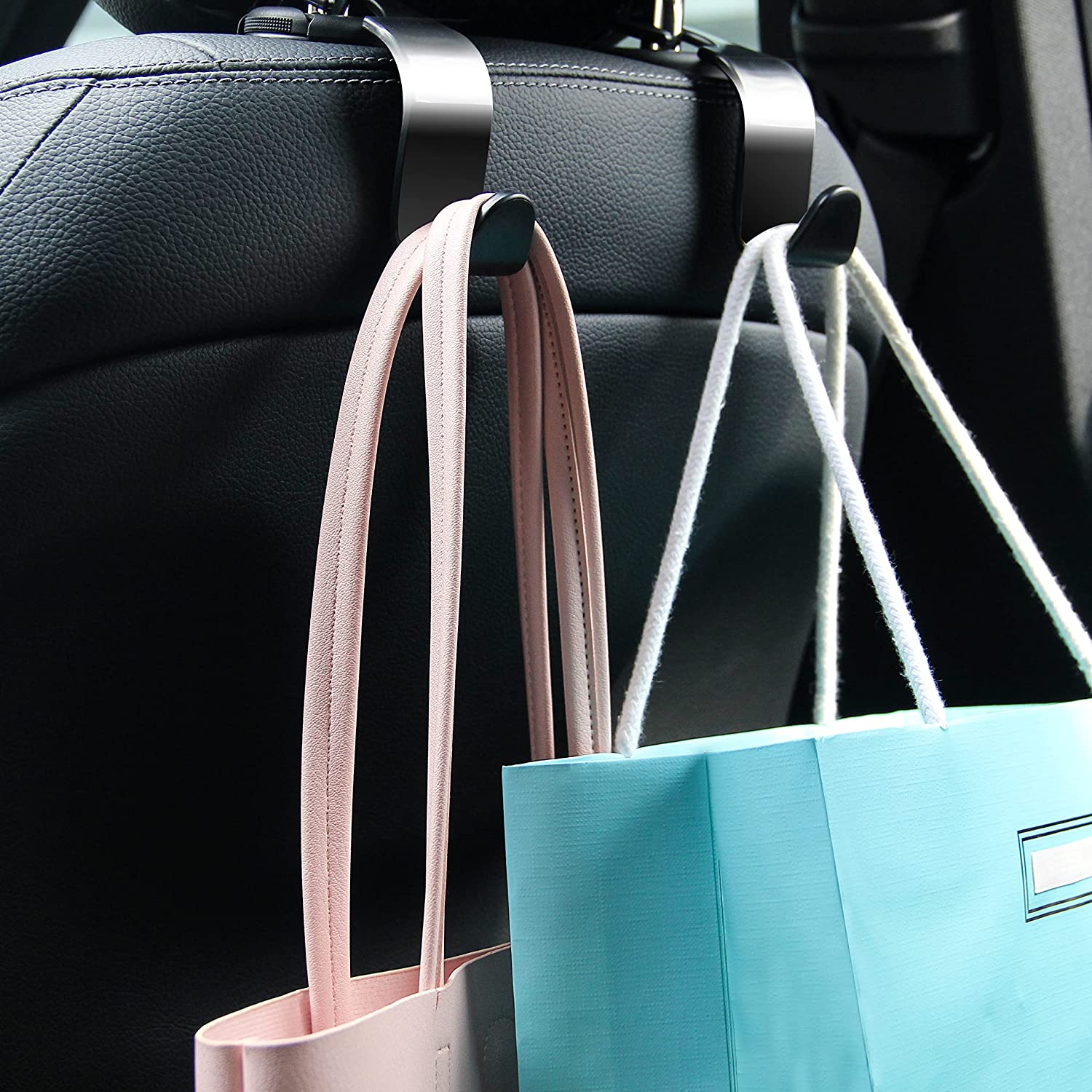 Ganchos multifuncionais pretos para assento de carro presos ao apoio de cabeça, segurando uma mala de mão e um saco de compras