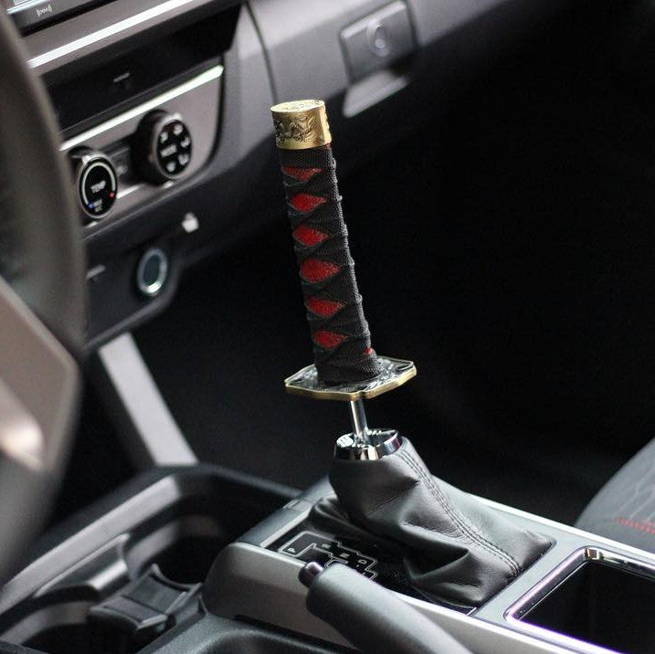 Interior de carro apresentando uma manete de mudanças única estilo katana com detalhes em vermelho, assemelhando-se a uma espada de samurai estilo jdm anime japão 